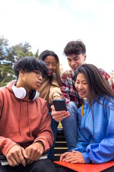 Group of multiracial happy young college student friends look at mobile phone. Teenagers using smartphone together outdoor. Vertical image. Youth lifestyle and social media addiction concept.