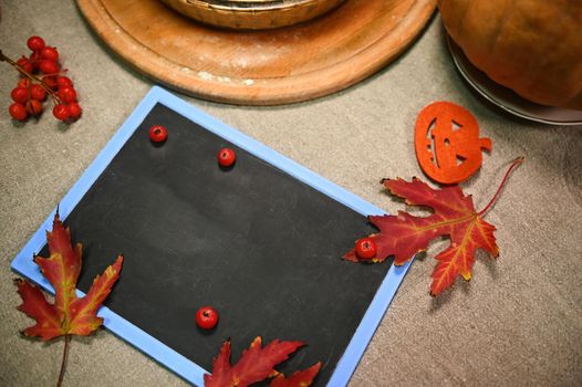 Top view of chalkboard with copy space for advertising text, next to dry autumn maple leaves, a branch of ripe viburnum berries, a pumpkin cut out of felt paper. Halloween and autumn holidays concept