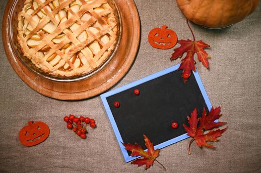 Top view: Blank blackboard with copy advertising space for promotional text, and freshly baked homemade classic American pumpkin pie with crispy crust lattice, for Thanksgiving Day on linen tablecloth