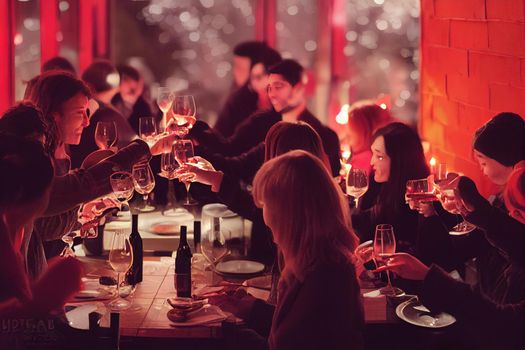 Happy friends group toasting red wine dining at restaurant terrace Young people socializing drinking and eating food sitting outside at winery bar table Winter season Dinner lifestyle concept. High quality illustration