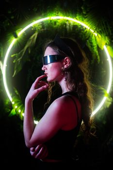 Caucasian woman in panoramic sunglasses against the background of an annular neon lamp in plants