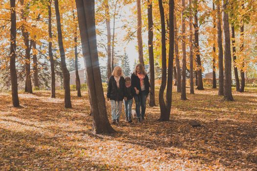 Grandmother and mother with granddaughter throw up fall leaves in autumn park and having fun. Generation, leisure and family concept