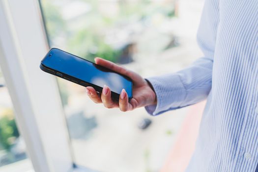 A modern mobile phone with a black screen is held in the hands of a woman, female hands with a smartphone close-up