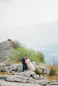 Groom hugs bride sitting on the stone top of the mountain. High quality photo