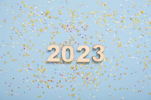 Wooden numbers 2023 on a pastel blue background with stars. Festive New Year background.