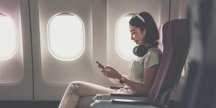 Joyful asian woman sits in the airplane and using mobile phone while go to travel.