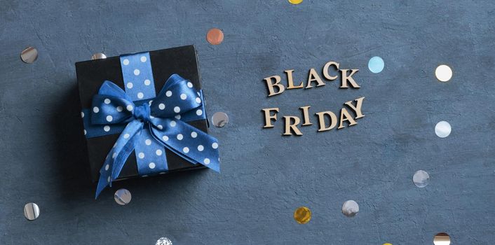 Black Friday text with black gift box flat lay on dark cement background. Top view.