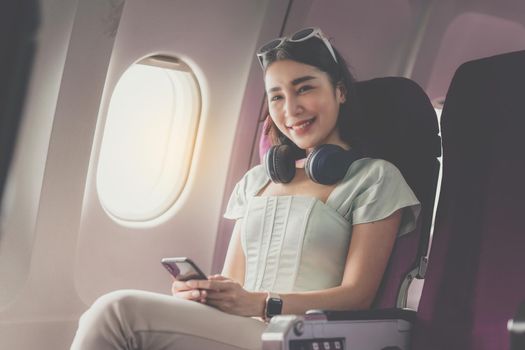 Joyful asian woman sits in the airplane and using mobile phone while go to travel.