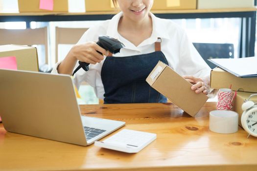 Female small online business owner holding scanner scanning parcel barcode tag before shipment at workplace. Woman selling products online, scanning parcel barcode. Online business concept.