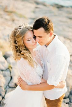 Bride and groom hug each other while standing on the rocks. High quality photo