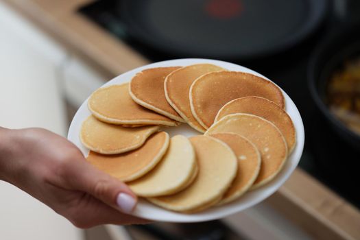 A woman's hand holds a plate of pancakes, close-up. Homemade fresh pastries for breakfast, traditional lunch