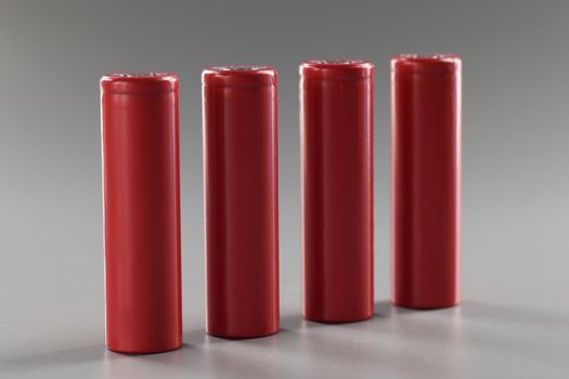 Red batteries stand in a row on a gray background, close-up. Rechargeable alkaline battery. Disposal lithium material