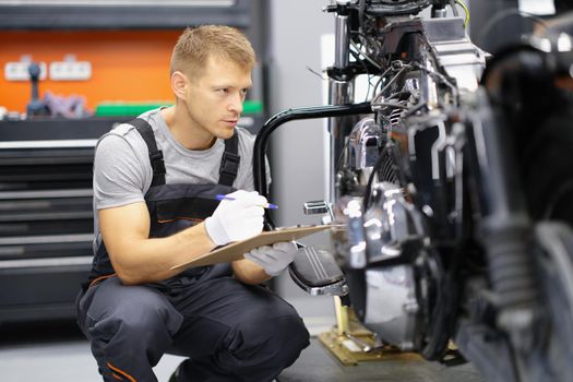 A man on a motorcycle takes notes, close-up. Checking the technical condition of the bike in the garage