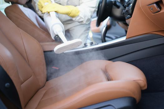 A man cleans a car interior with a steam cleaner, close-up, blurry. Antibacterial treatment upholstered transport