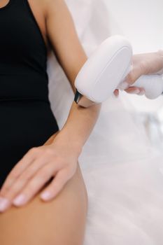 Cosmetology. Beautiful woman receiving laser hair removal procedure at beauty salon. Beautician doing beauty treatment for female arm at spa salon.