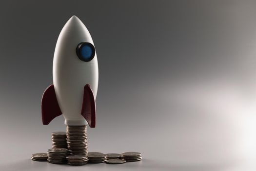 Plastic rocket on top of a stack of coins on a gray background. The concept of economic growth, project start