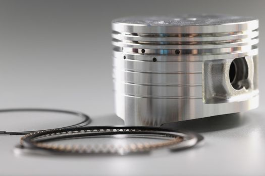 Silver mechanical round part of the engine piston on a gray background, close-up. New shiny auto detail, repair