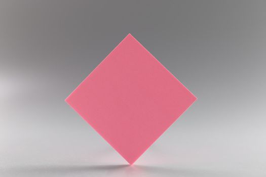 Pink blank paper rhombus on a gray background, close-up. beautiful design element, sheet sticker, branding