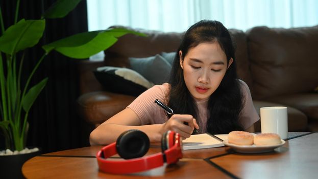 Concentrated young woman doing homework or making agenda plan planning daily appointment on notebook.