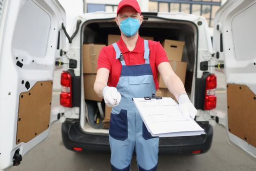 A male courier holds out documents for signature. Delivery of parcels around the city during a pandemic
