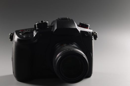 Black photo camera on a gray background, close-up. Digital device for photography, professional equipment for photographer