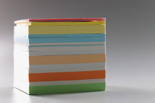 Multi-colored stack of paper for notes on a gray background, close-up. Different color blank post notes