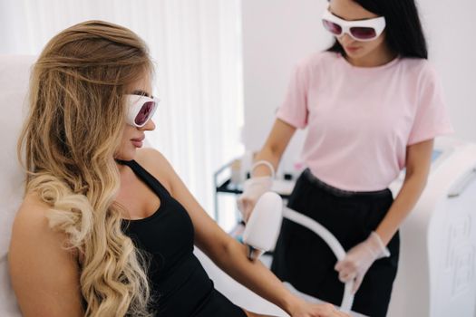 Cosmetology. Beautiful woman receiving laser hair removal procedure at beauty salon. Beautician doing beauty treatment for female arm at spa salon.