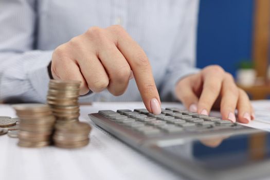 A woman in the office counts on a calculator near the coins, hands close-up. Payment of interest on a deposit