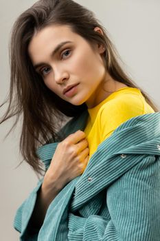 Beauty portrait of dark haired woman with perfect skin looking at camera, wearing casual style jacket and yellow shirt. Indoor studio shot isolated on gray background.
