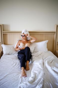 A beautiful young woman is lying in a large snow-white bed with a towel on her head.