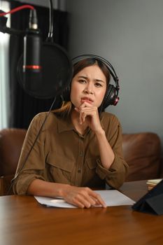Concentrated female radio host listening to interesting conversation with guest during streaming podcast in home studio.