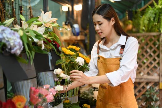 Asian woman florist wearing apron arranging flowers at her rustic flower shop. Business, sale and floristry concept.