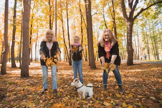 Grandmother and mother with granddaughter throw up fall leaves in autumn park and having fun. Generation, leisure and family concept