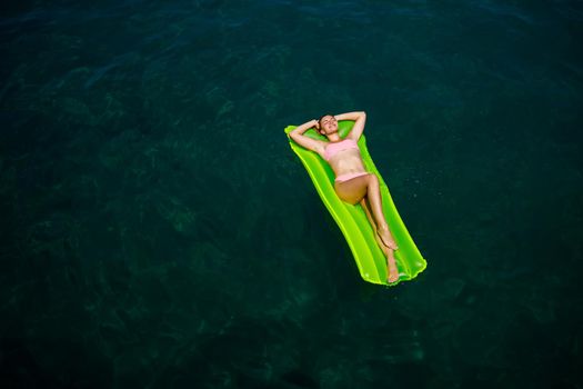 A young woman in a swimsuit swims on an inflatable bright mattress in the sea. Summer vacation concept.