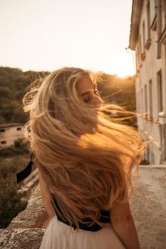 Blonde long hair, nature summer happy adult girl with long blond hair developing in the wind in nature. Dressed in a black top, white skirt