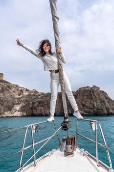 Woman standing on the nose of the yacht at a sunny summer day, breeze developing hair, beautiful sea on background.