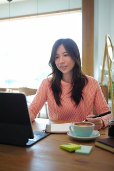 Charming asian woman in pink sweater working with computer tablet.