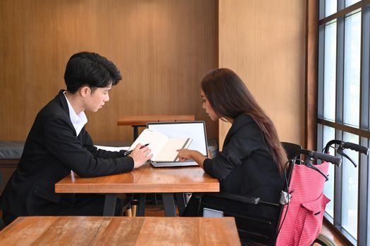 Businesswoman in a wheelchair discussing business documents with her colleague.