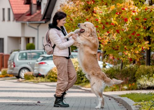 Preteen young woman in pink jacket with golden retriever dog smiling at street. Pretty woman with pet doggy labrador spend autumn time outdoors
