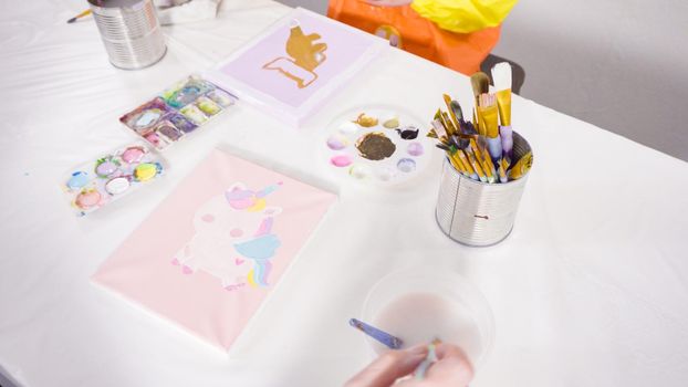 Little girl painting with acrylic paint on canvas with her mother for a distant learning art project.