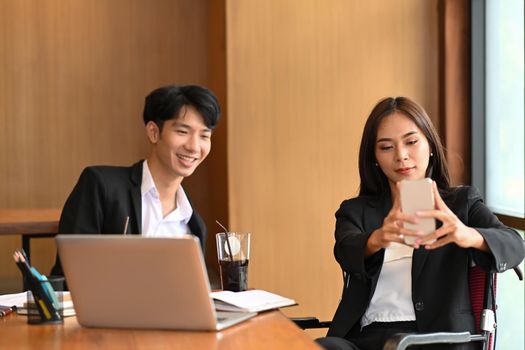 Businesswoman with disability in wheelchair using smart phone with colleague in office.