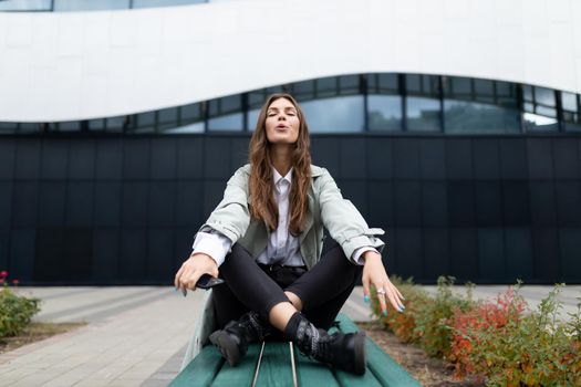 young woman sitting in yoga pose in park resting during work break near office.