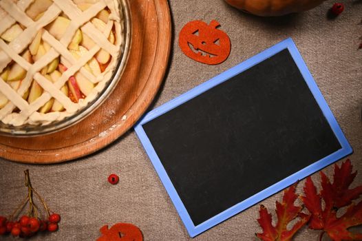 Top view. Still life with a American classic freshly baked Thanksgiving pie with pumpkin, apples, and crispy crust lattice on a wooden board next to a blackboard with copy space for advertising text