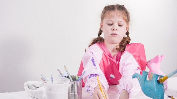 Little girl painting paper mache figurines with acrylic paint for her homeschooling art project.