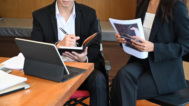 Office workers and person in a wheelchair working together in office.