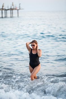Portrait of a beautiful woman in a black swimsuit with blond hair posing on the beach by the sea. Young woman walking on the beach