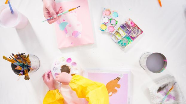 Flat lay. Little girl painting with acrylic paint on canvas with her mother for a distant learning art project.