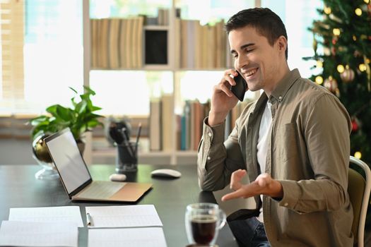 Handsome man working with laptop computer and talking on mobile phone.