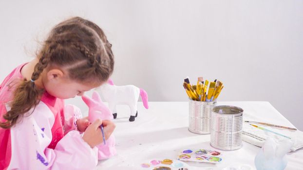 Little girl painting paper mache figurines with acrylic paint for her homeschooling art project.