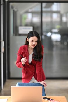 Beautiful businesswoman standing at office desk and looking at laptop computer.